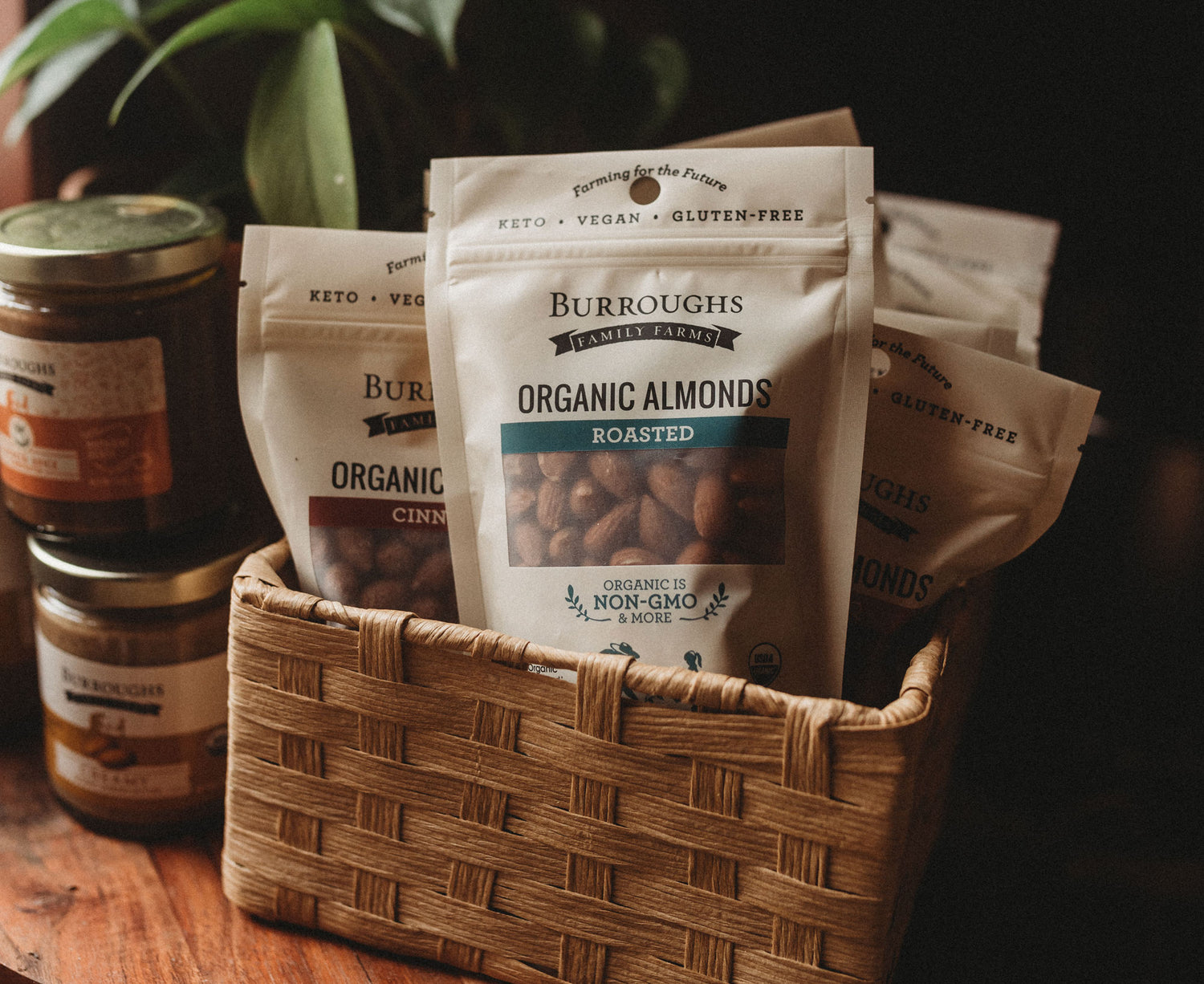 Box of Burroughs Family Farm organic almonds in packaging with small jars of organic almond butter stack by its side