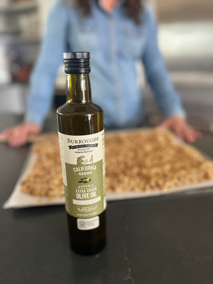 Woman standing behind a tray of almonds with a bottle of olive oil in front