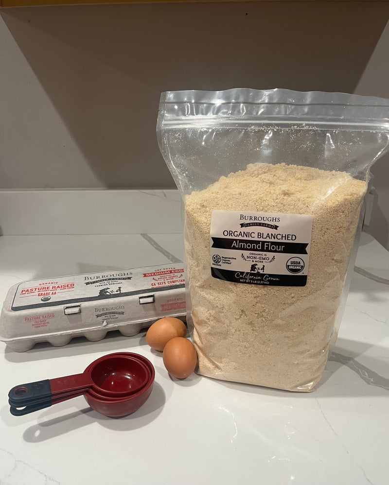 Bag of Burroughs Family Farms Organic Blanched Almond Flour on a kitchen counter with eggs and measuring spoons