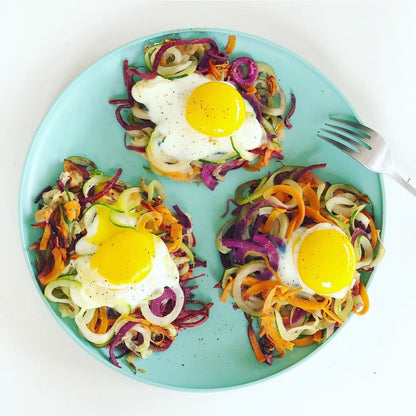 Three fried eggs on nests of vegetable noodles on a blue plate