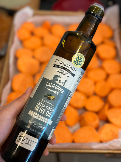 Hand holding a bottle of Koroneiki olive oil above a crate of citrus