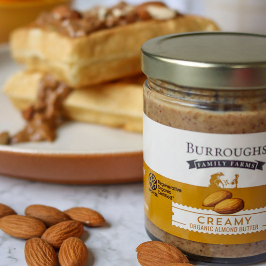 Photo of the Burroughs Family Farm creamy almond butter with almond butter topped Belgium waffles in the background
