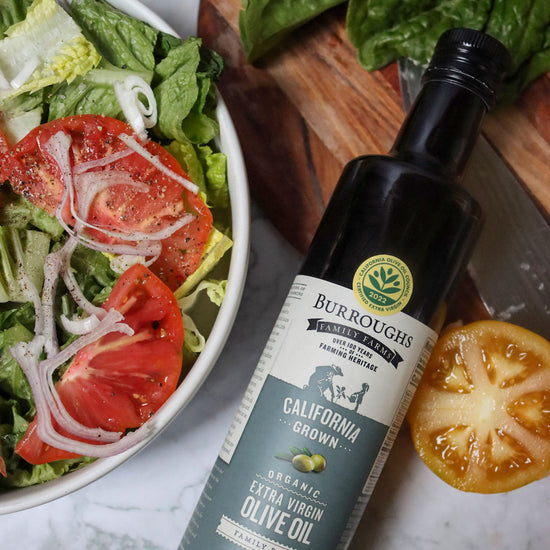 Photo featuring the Burroughs Family Farm Organic Extra Virgin Olive Oil next to a large salad